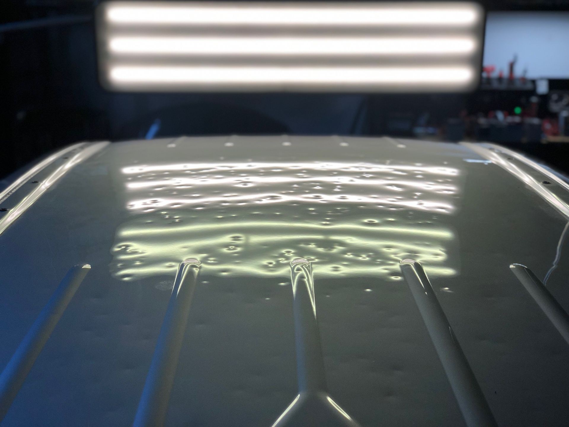 Close-up of a car roof with dent reflections under bright overhead lights.